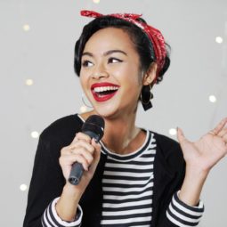 Wanita asia dengan rambut hitam menggunakan gaya rambut pin up hair dengan scarf merah sedang bernyanyi menggunakan mikrofon