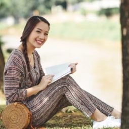 Wanita asia dengan model rambut french braid samping membaca buku di pinggir sungai