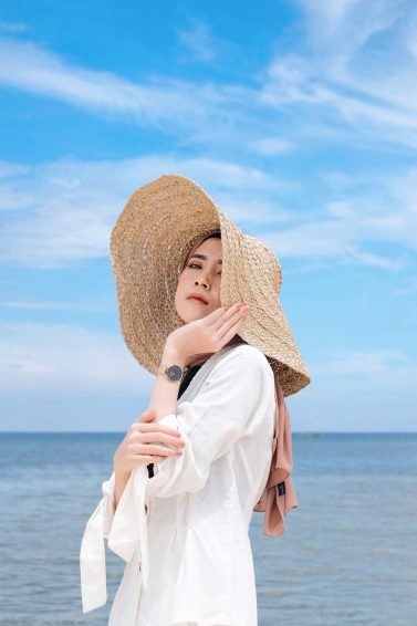 hijab berpose memegang topi yang dia kenakan di pantai