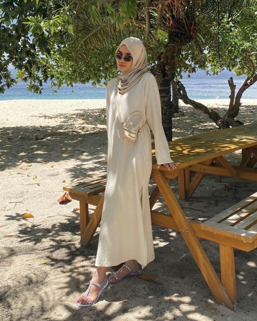 wanita hijaber memakai dress dan kacamata berdiri di pantai