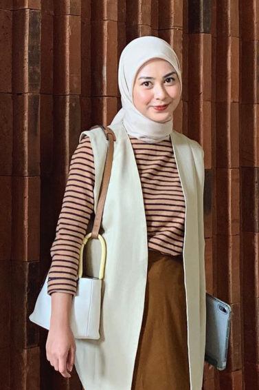 Selebgram hijab Dianty berdiri mengenakan baju motif stripes dan rok panjang warna cokelat dengan blazer dan hijab warna krem.