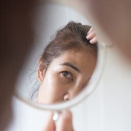 wanita asia sedang melihat cermin dan memperhatikan kulit kepala