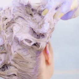 wanita dengan rambut pirang sedang keramas dengan purple shampoo atau shampoo ungu