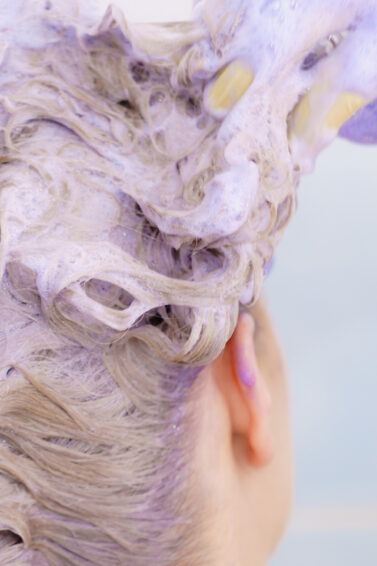 wanita dengan rambut pirang sedang keramas dengan purple shampoo atau shampoo ungu