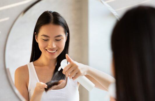 Wanita Asia dengan menyemprotkan serum atau vitamin rambut pada ujung rambut
