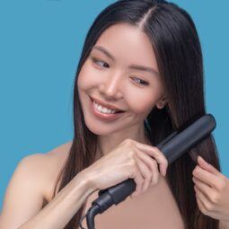 Wanita Asia berambut panjang sedang mencatok rambut