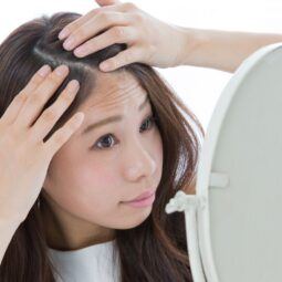 Wanita Asia sedang bercermin sambil memegang kepala dan rambut.