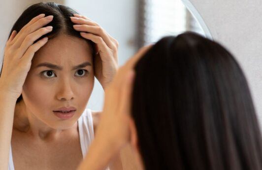 Wanita Asia sedang bercermin memeriksa kulit kepalanya.