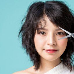 Wanita Asia sedang memegan gunting ingin memotong rambut sendiri.