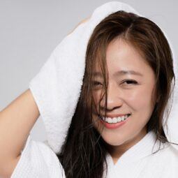 Wanita Asia sedang mengeringkan rambut menggunakan handuk warna putih.
