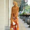 Wanita Indonesia kenakan baju warna cokelat peanut dan hijab warna kuning mustard.