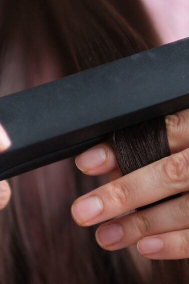 Foto dari dekat wanita sedang mencatok rambut menggunakan catok rambut.