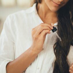Wanita berambut panjang sedang mengaplikasikan minyak esensial pada rambut.