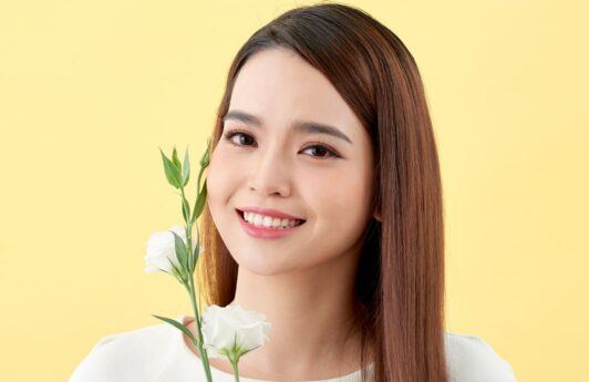 Wanita Asia sedang tersenyum sambil memegang bunga putih