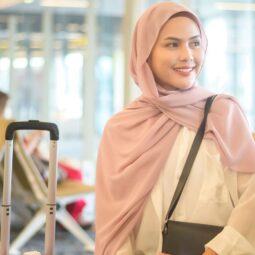 Wanita Asia mengenakan hijab pashmina warna pink sedang duduk menunggu pesawat