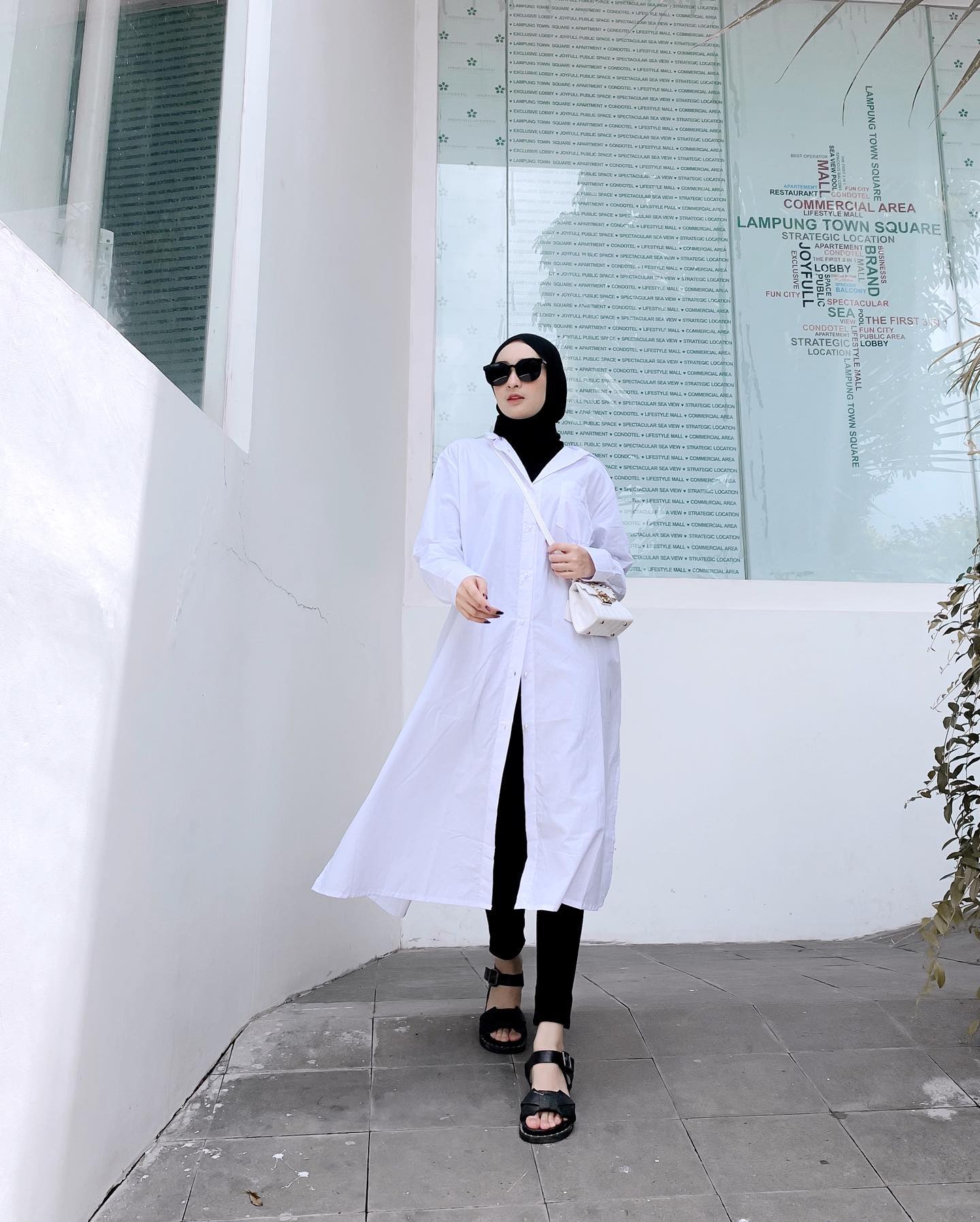 Wanita Indonesia berdiri mengenakan baju tunik putih dan legging hitam.
