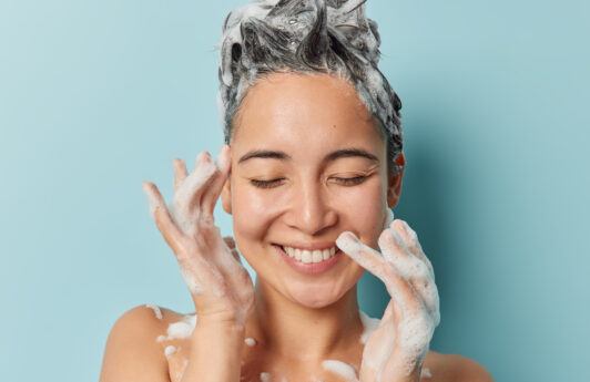 Wanita Asia sedang keramas dengan shampoo dengan wajah tersenyum.