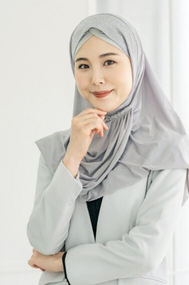 Wanita Asia sedang berpangku tangan mengenakan hijab warna abu-abu dan blazer warna putih.