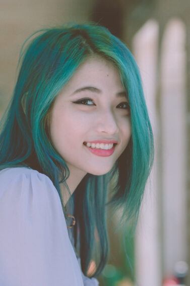 Wanita Asia dengan warna rambut hijau tosca sedang tersenyum