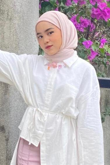 Wanita Indonesia memakai hijab instan warna nude dengan kemeja putih berpotongan asimetris.