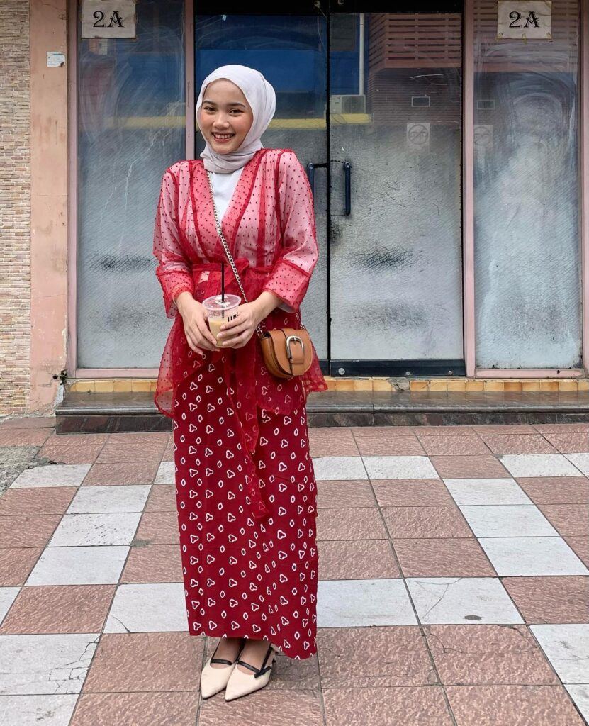 Selebgram Indonesia berhijab mengenakan baju atasan putih, luaran sheer warna merah dan rok batik warna merah.