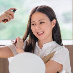 wanita asia sedang menyemprotkan spray rambut di depan cermin