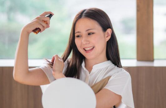 wanita asia sedang menyemprotkan spray rambut di depan cermin