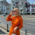 Wanita kaukasia kenakan baju warna orange dan hijab warna cokelat susu.