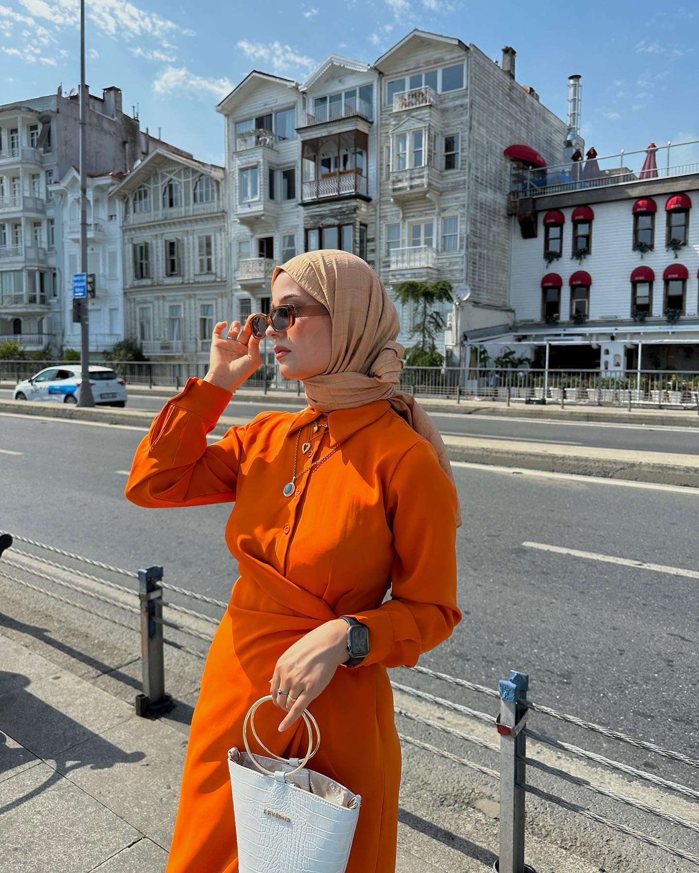 Wanita kaukasia kenakan baju warna orange dan hijab warna cokelat susu.