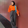 Wanita Indonesia pakai kemeja warna orange, celana panjang abu-abu dan hijab pashmina warna hitam.