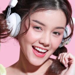 Wanita Asia menggunakan headphone warna putih sedang tertawa gembira dengan kedua tangan memegang rambut.