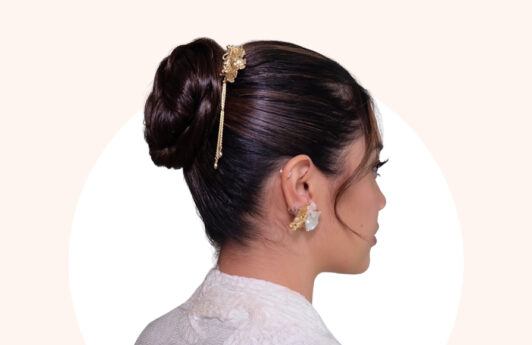 Wanita Asia dengan gaya rambut cepol kepang yang diberikan aksen poni menjuntai dan aksesori rambut warna emas.