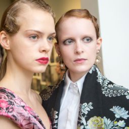 Dos mujeres de peinado recogido con gel, una tiene el rostro más visible y lleva una especie de orquídea metálica