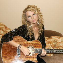 Taylor Swift con cabello rubio, suelto, muchos rulos, raya al costado
