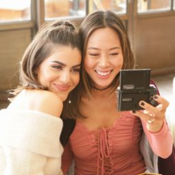 Dos mujeres castañas, de cabello lacio sacándose una selfie