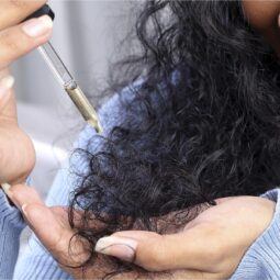 mujer de pelo largo negro con rulos aplicando aceite en las puntas, aceites naturales para el pelo