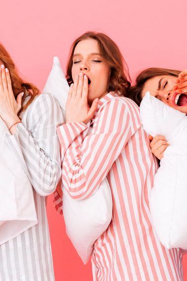 tres mujeres en pijamas a rayas con almohadas y pelo suelto, dormir con pelo atado o suelto