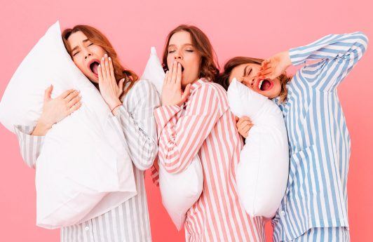 tres mujeres en pijamas a rayas con almohadas y pelo suelto, dormir con pelo atado o suelto