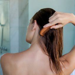 mujer desnuda de espaldas peinado su pelo húmedo luego de aplicar aceite de argán para el pelo