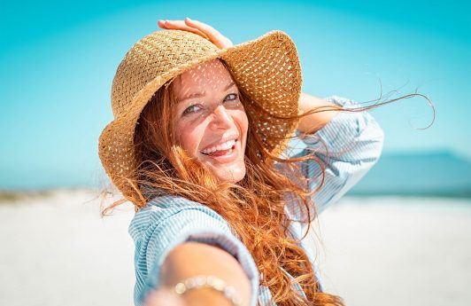 mujer pelirroja de pelo largo con ondas sonriente con sombrero