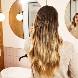 mujer rubia de pelo largo mirándose al espejo del baño, pelo graso