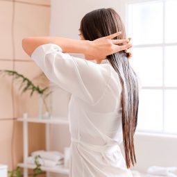 mujer de pelo largo lacio color castaño de espaldas aplicando aceite sobre el pelo, aceite de oliva para el pelo