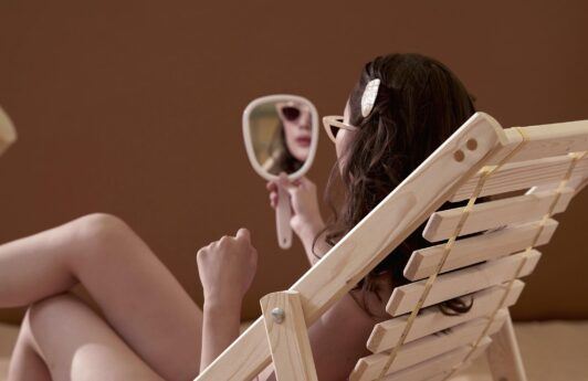 mujer sentada en reposera en la playa con espejo en mano, por que se cae el pelo en verano