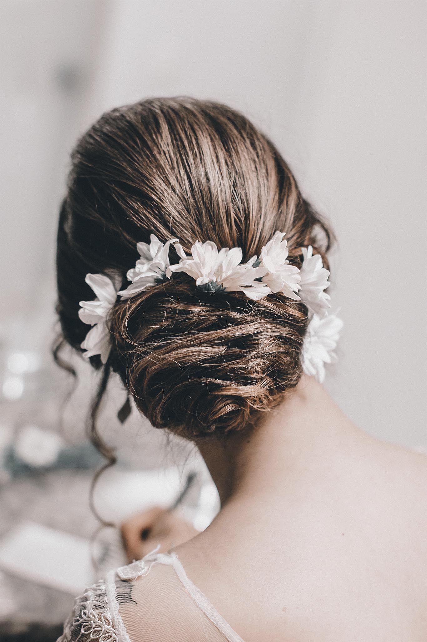 mujer de espaldas vestida de novia con chignon hecho con mechones cruzados y flores, peinados para casamiento