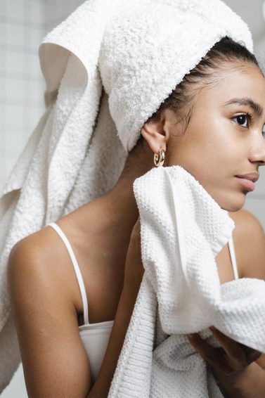 mujer con toalla en la cabeza frente al espejo, shampoo sin sal