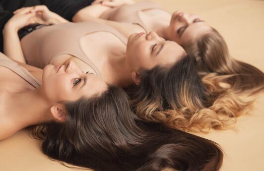 tres mujeres recostadas sobre el suelo con el pelo suelto, como eliminar la caspa