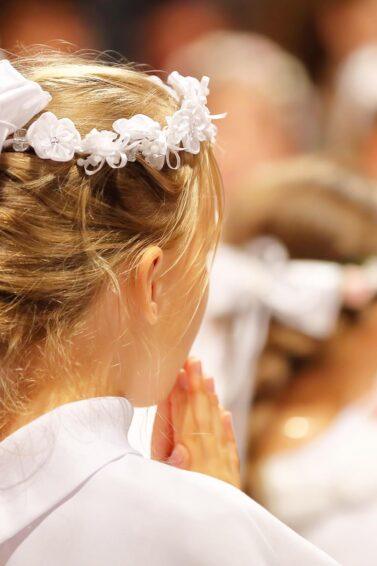 detalle de peinado de niña en primera comunión con trenza francesa y corona con flores, moño y cintas, peinados para comunión