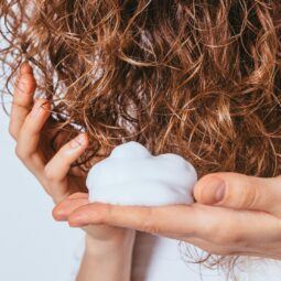 detalle de mano de mujer aplicando mousse para el pelo sobre cabello con ondas