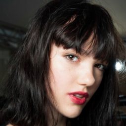 Short hairstyles for thick hair: Model backstage at fashion show with her dark brown hair in a long bob with bangs. Model is wearing a black top and soft red lipstick.