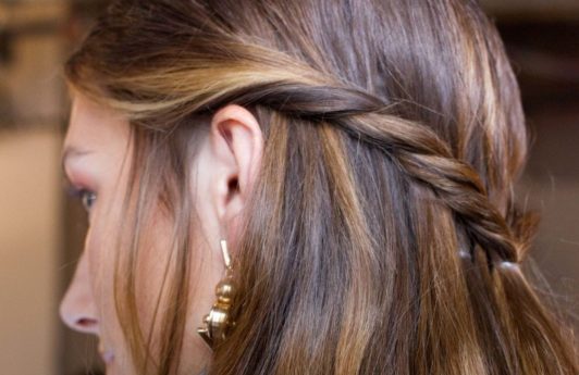 Medium hairstyles: Woman with brown highlighted straight hair in twisted half-up, half-down hairstyle.